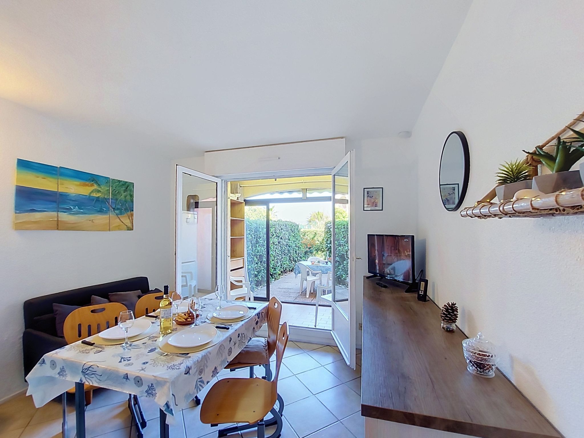 A dining area with a table set for four, a sofa, a TV, and a painting on the wall.