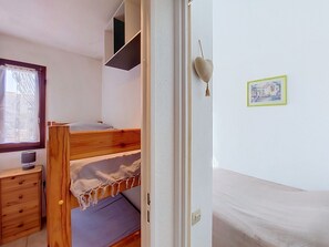 A bunk bed with a wooden headboard, a small desk with a lamp, a window with curtains, and a framed picture on the wall. - Le Tropique by Interhome (Saint Cyprien)