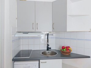 Een keuken met witte kastjes, een zwart aanrecht, een roestvrijstalen spoelbak en een mand met fruit.
