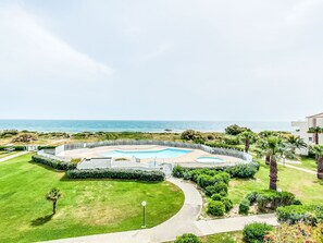 A pool area with a view of the sea, surrounded by greenery and palm trees. - Les Goelettes by Interhome (Saint Cyprien)
