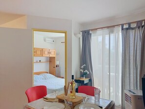 Een hotelkamer met een bed, een houten garderobe, een eettafel met stoelen, een bijzettafeltje met een fles en glazen, en een raam met gordijnen.