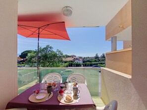 A balcony with a table set for two, a red umbrella, and a view of a residential area. - Les Goelettes by Interhome (Saint Cyprien)