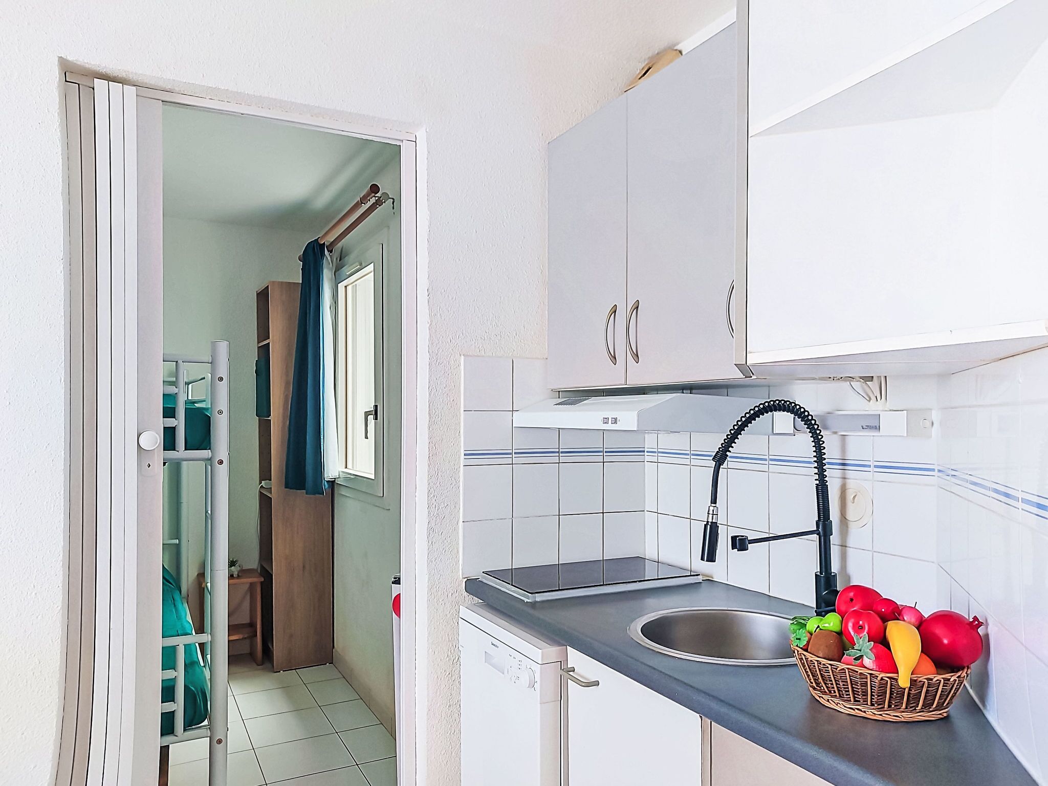 A compact kitchen with a sink, cabinets, and a basket of fruit.