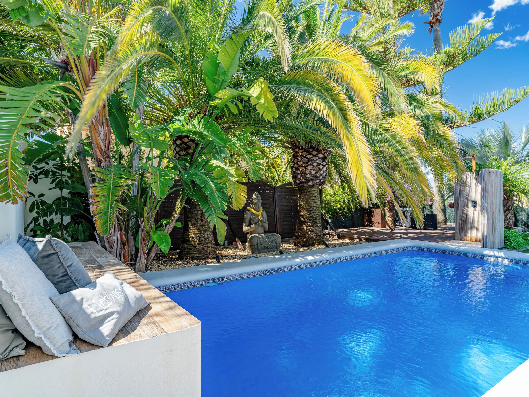 A swimming pool surrounded by tropical plants and a stone statue.