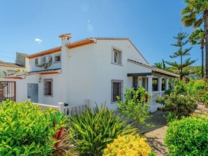 A white two-story house with a tiled roof, a small porch, and a garden with various plants. - Villa La Calma by Interhome (Jávea)