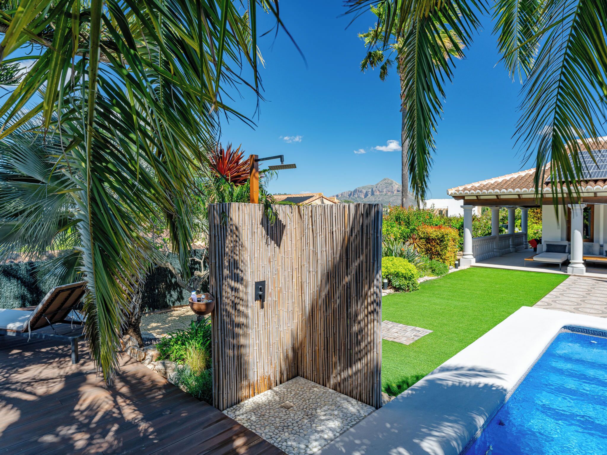 A pool area with a wooden fence, a covered seating area, and a well-maintained lawn.