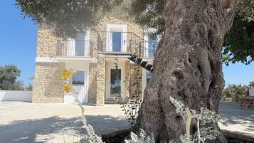 Un edificio in pietra con un balcone, immerso tra alberi e piante.