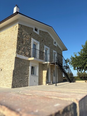 A two-story stone building with a balcony, a staircase, and a door.