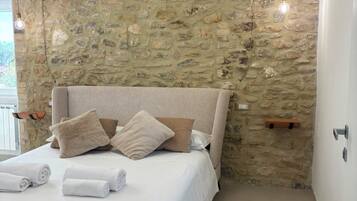 Un dormitorio con pared de piedra, cama con ropa de cama blanca y una lámpara de araña moderna.