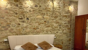 A bedroom with a stone wall, a bed with white bedding, two brown pillows, and a wooden wardrobe. - Tenuta Ferrante Relais (Abruzzo)