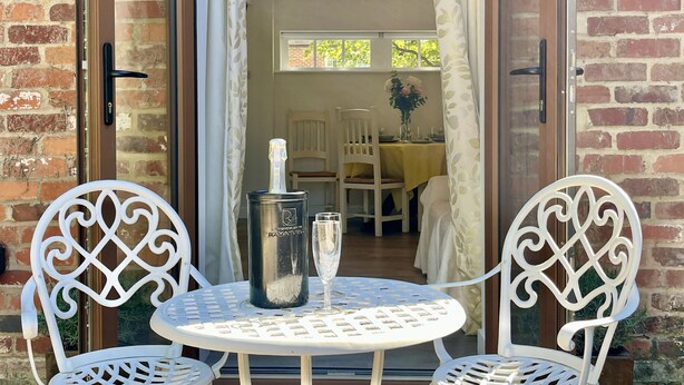 Un patio con dos sillas de metal blanco y una mesa, una botella de champán y una copa sobre la mesa.