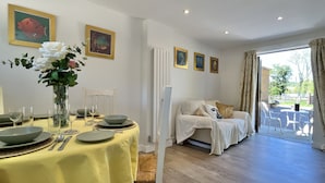 Un comedor con una mesa preparada para cuatro, un sofá al fondo y vistas al exterior a través de un ventanal.