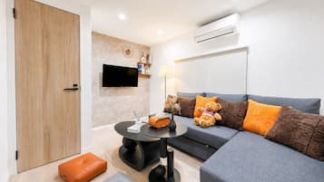 A modern living room with a grey sofa, orange and brown cushions, a round black table, and a television mounted on the wall.