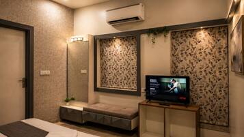 A modern hotel room with a bed, a seating area, a TV, and an air conditioning unit.