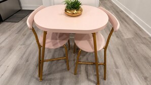 A round table with a gold base and pink chairs, a small potted plant on the table, and a light-colored wooden floor. - Pink Luxe Retreat In Downtown Dallas (Dallas)