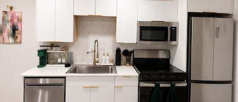 A modern kitchen with white cabinetry, stainless steel appliances, and a green rug.