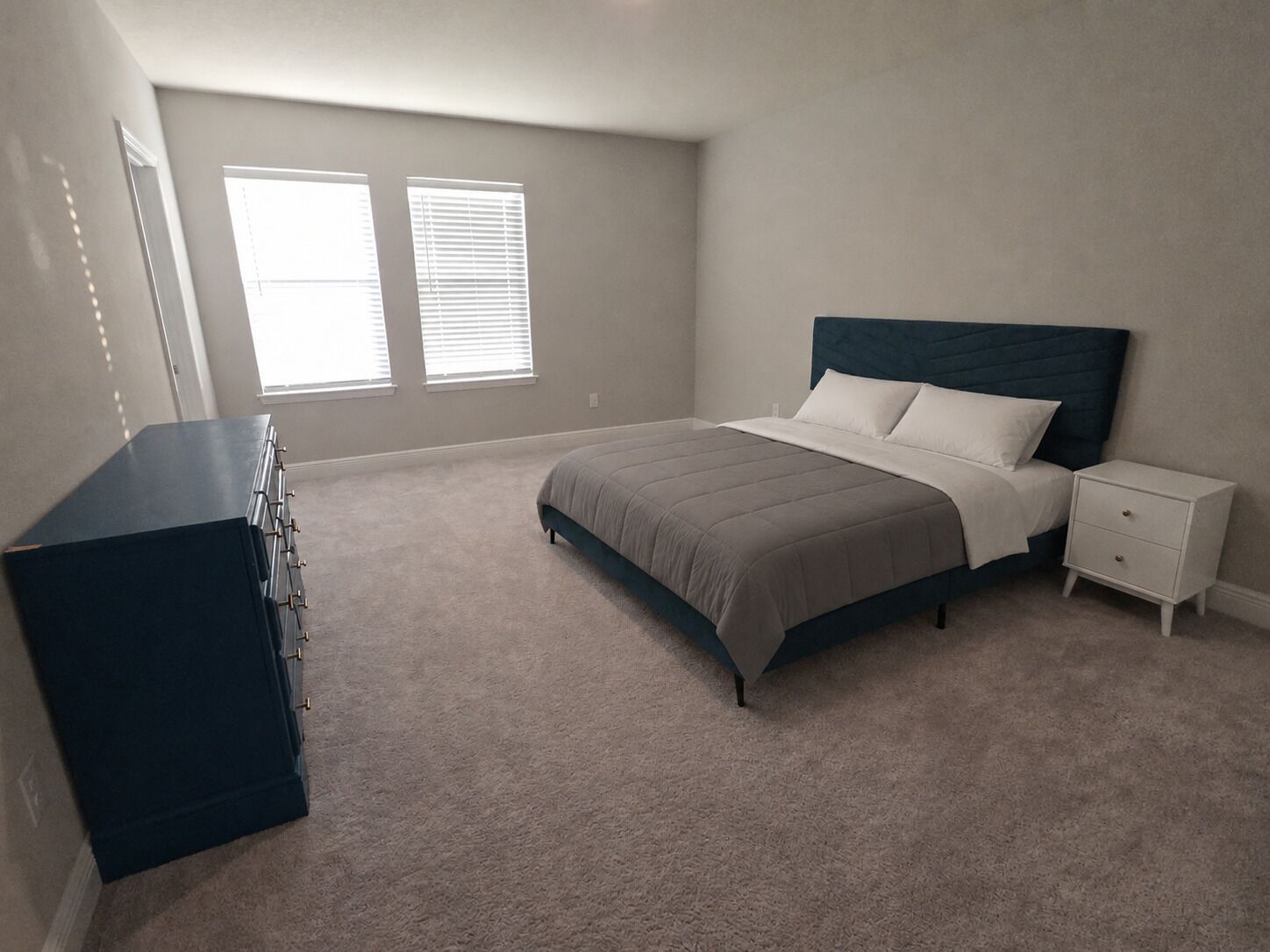 A bedroom with a bed, dresser, nightstand, and two windows.