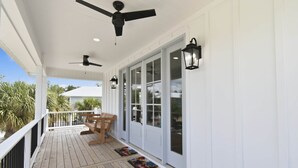 Une véranda couverte avec une terrasse en bois, des ventilateurs de plafond, des portes blanches et une vue sur l’extérieur.