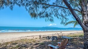 Una spiaggia con sedie e un tavolo di legno, un albero e vista sull'oceano.