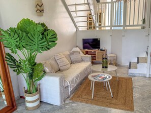Ein Wohnzimmer mit einer Couch, einem Couchtisch, einem Fernseher und einer großen Pflanze.