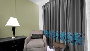Ein Zimmer mit einem Sessel, einer Lampe, einem Tisch mit Muster und Vorhängen in Blau und Grau.