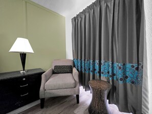 A room with a chair, a lamp, a patterned table, and curtains with a blue and grey design.