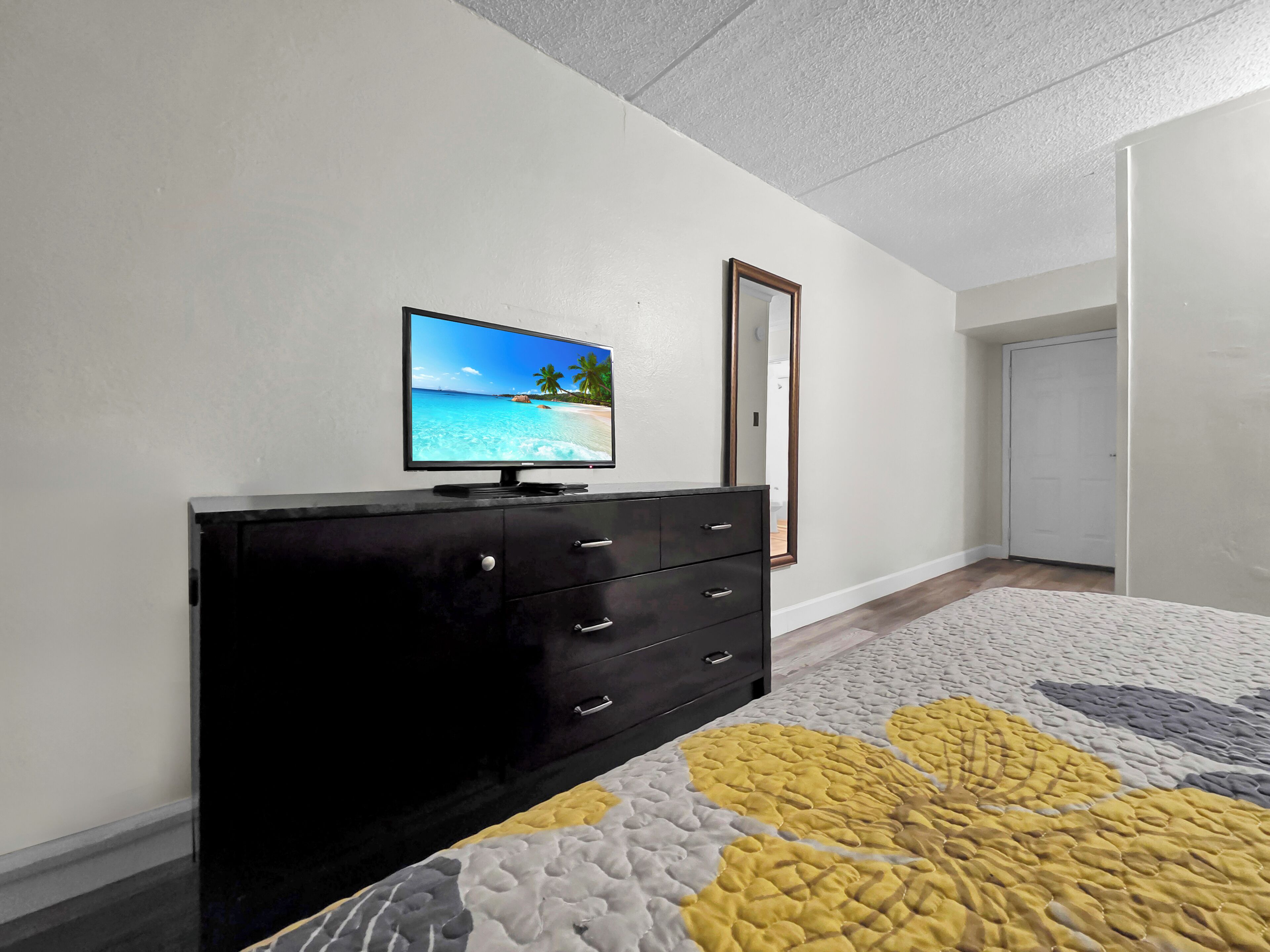 A bedroom with a bed, a dresser, a television on the wall, and a door.