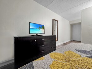 A bedroom with a bed, a dresser, a television on the wall, and a door.