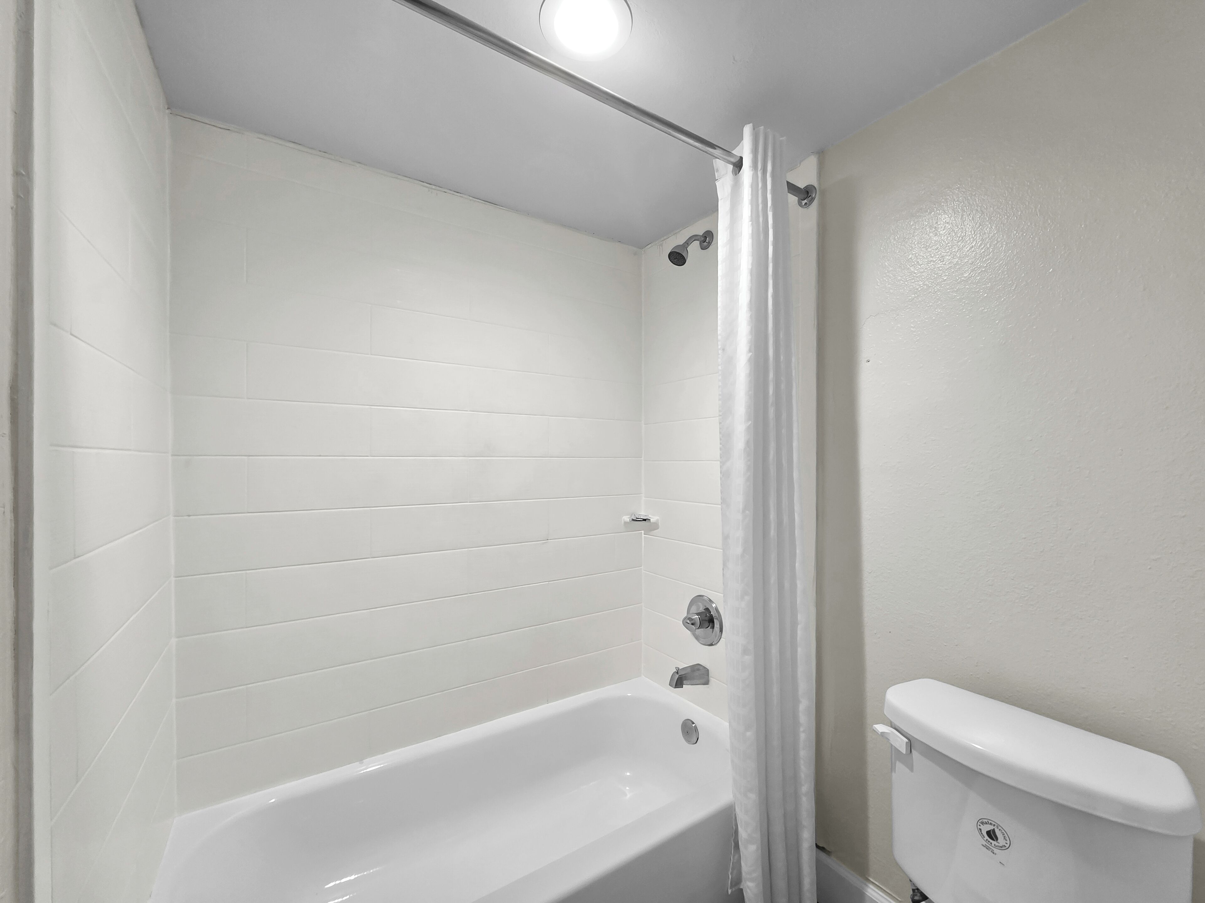 A bathroom with white tiled walls, a white bathtub, and a white toilet.