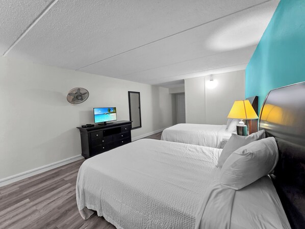 A hotel room with two beds, a TV, a mirror, a lamp, and a fan.
