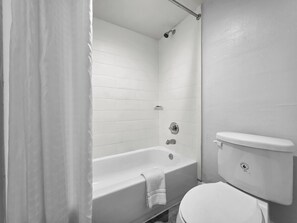 A bathroom with a white bathtub, a toilet, and a shower area.