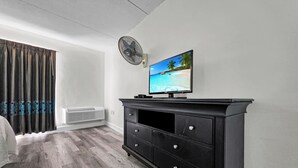Een slaapkamer met een bed, een televisie op een zwarte dressoir, een plafondventilator en een raam met gordijnen.