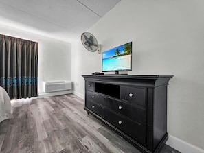 A bedroom with a bed, a TV on a black dresser, a ceiling fan, and a window with curtains.