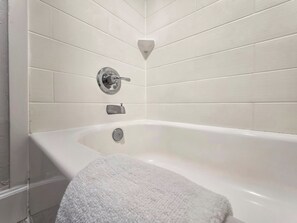 A bathroom with a white bathtub, a towel, and a wall-mounted faucet.