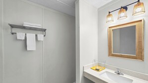 Ein modernes Badezimmer mit Dusche, einem weißen Waschbecken mit goldener Spiegelrahmung und einem Handtuchhalter mit drei Handtüchern.