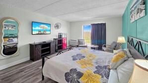 Ein Hotelzimmer mit Bett, Schreibtisch, Stuhl, Spiegel, Ventilator und einem fensterbepflanzten Fenster.