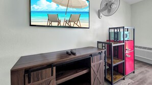 Une pièce décorée d’un tableau sur le thème de la plage, avec un ventilateur, un réfrigérateur rouge et un bureau en bois.