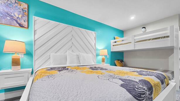 A bedroom with a bed, white nightstands, a white headboard, a bunk bed, and a teal accent wall. - Crystal Palace Resort - Family Suite King (Port Bolivar)