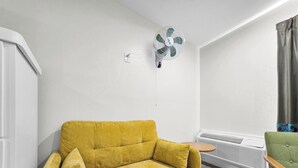 A yellow sofa, a green chair, a white wall, a white ceiling fan, and a white radiator. - Crystal Palace Resort - Family Suite King (Port Bolivar)