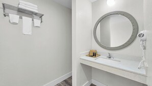 A bathroom with a white sink, a round mirror with a light, and a towel rack with towels.