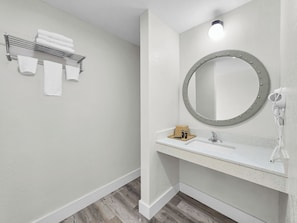 A bathroom with a white sink, a round mirror with a light, and a towel rack with towels.