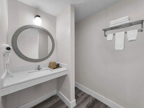 A bathroom with a round mirror, a hairdryer, a towel rack, and a sink.