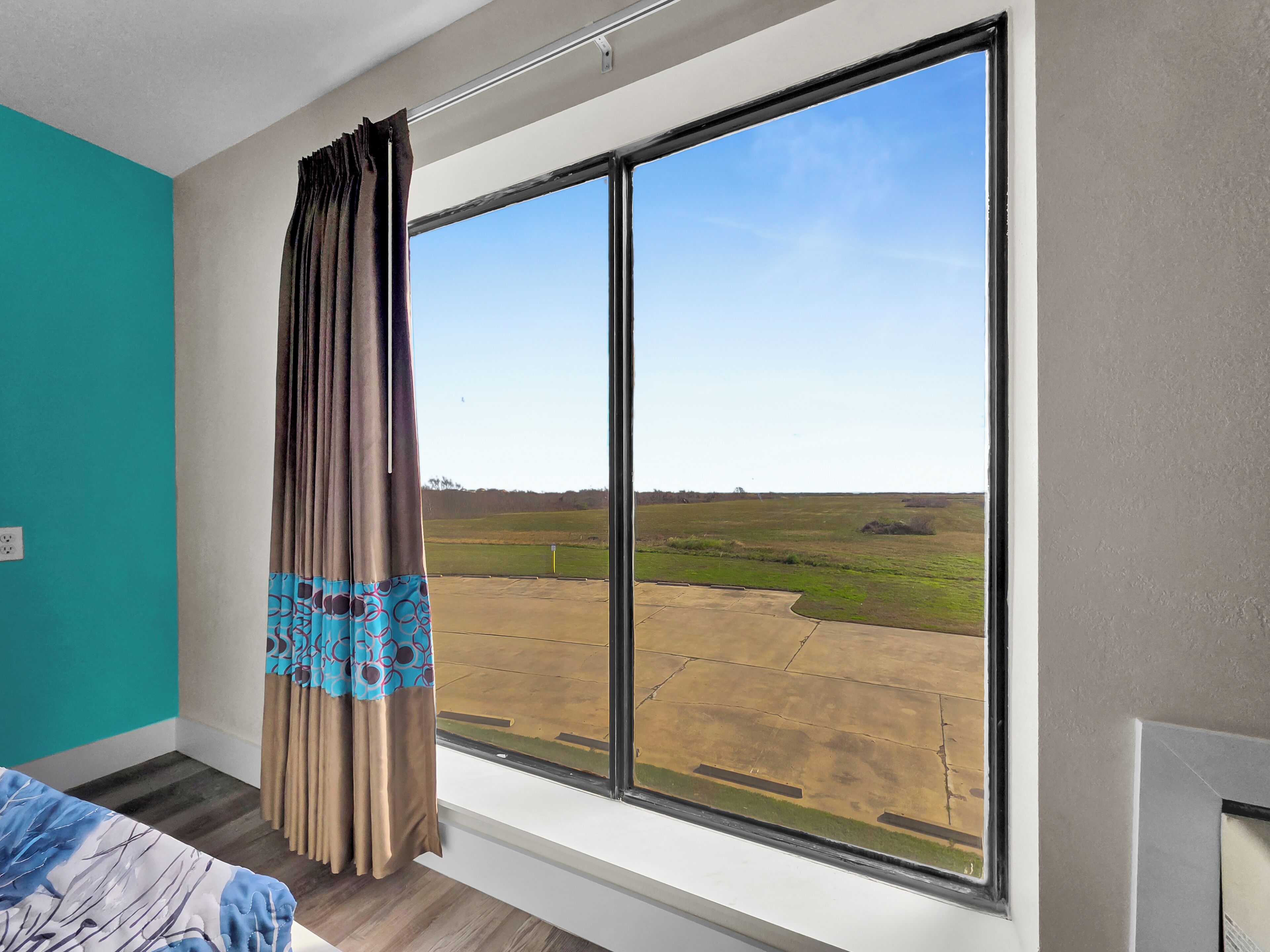 A room with a large window, a bed with a patterned bedspread, and a view of a grassy field.