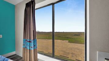 A room with a large window, a bed with a patterned bedspread, and a view of a grassy field.