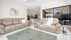 Una sala de estar moderna con dos sofás beige, un tapiz verde estampado y un ventilador de techo.