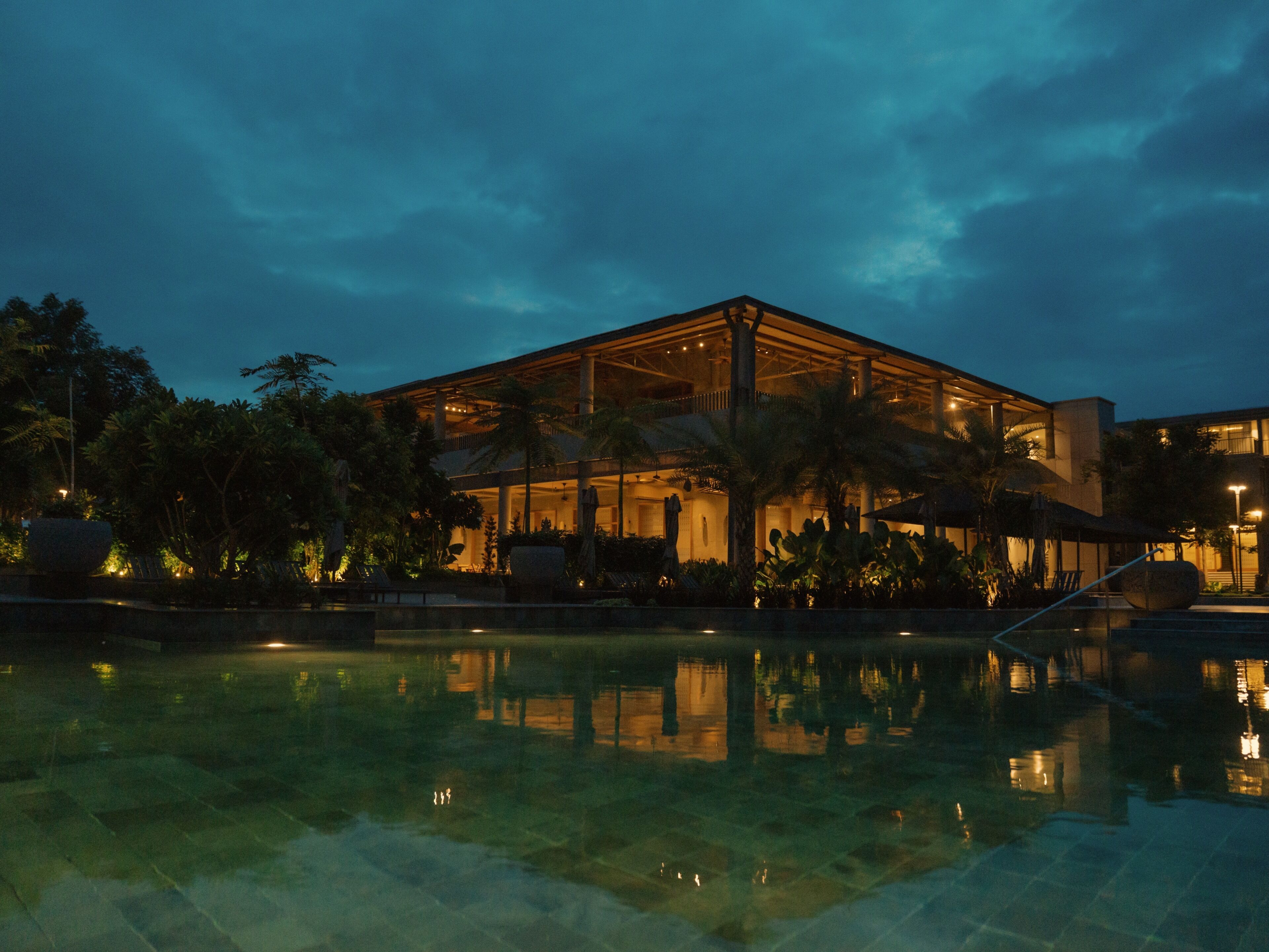 A modern hotel with a glass facade, a pool, and palm trees.