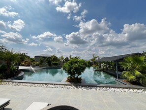 A swimming pool with a clear sky, surrounded by greenery and a covered area. - Arth Resorts (Hyderabad)