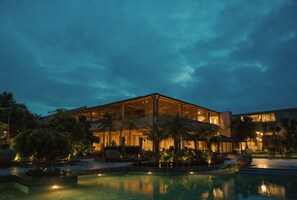 Un edificio moderno con piscina, rodeado de palmeras y plantas.