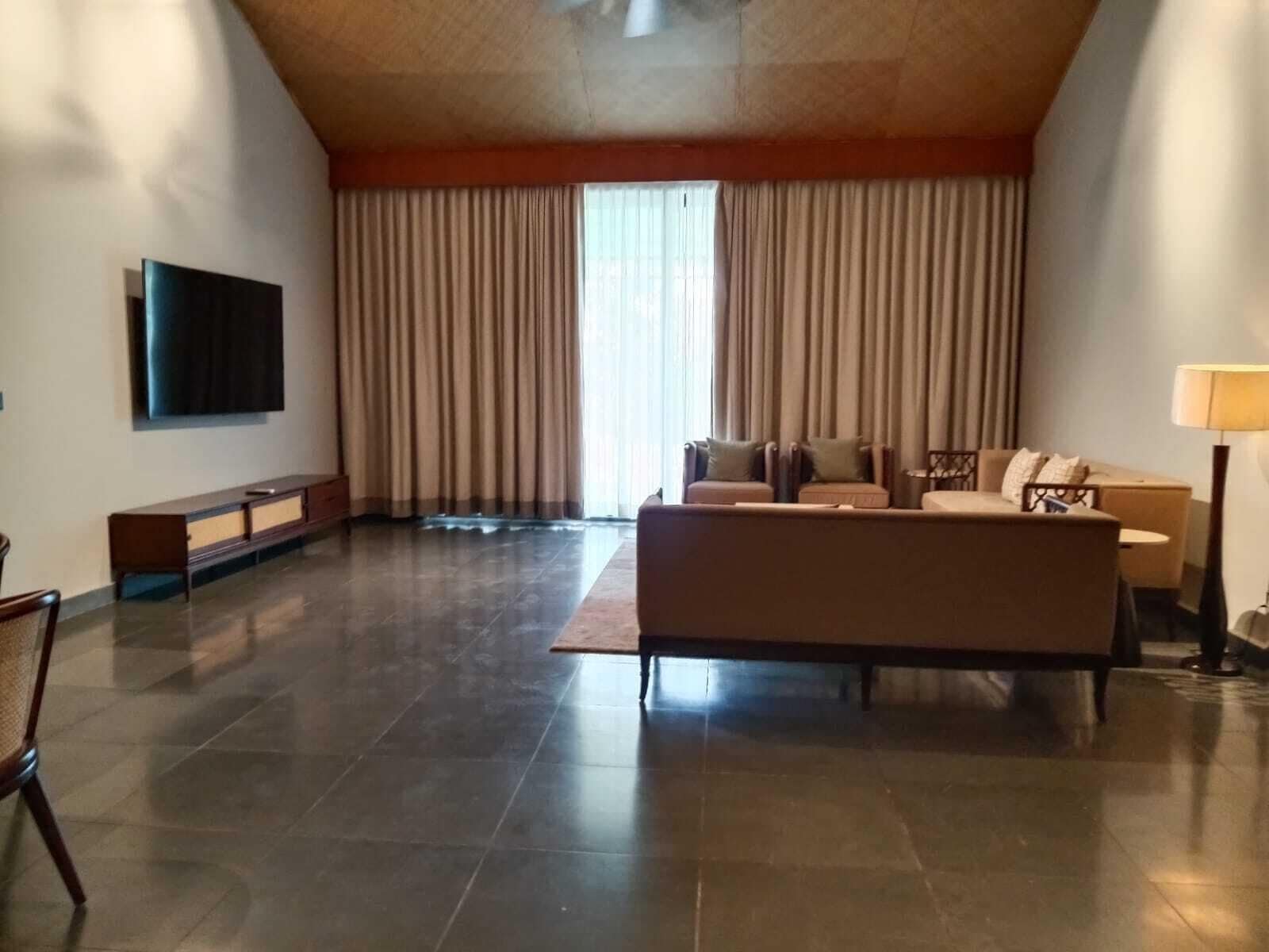 A spacious living room with a large flat-screen TV, a sofa set, a coffee table, and a lamp.
