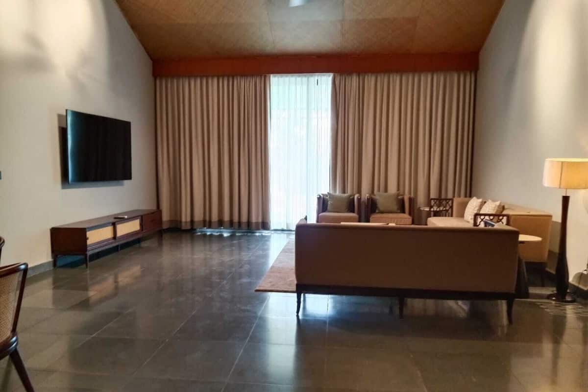 A spacious living room with a large flat-screen TV, a sofa set, a coffee table, and a lamp.